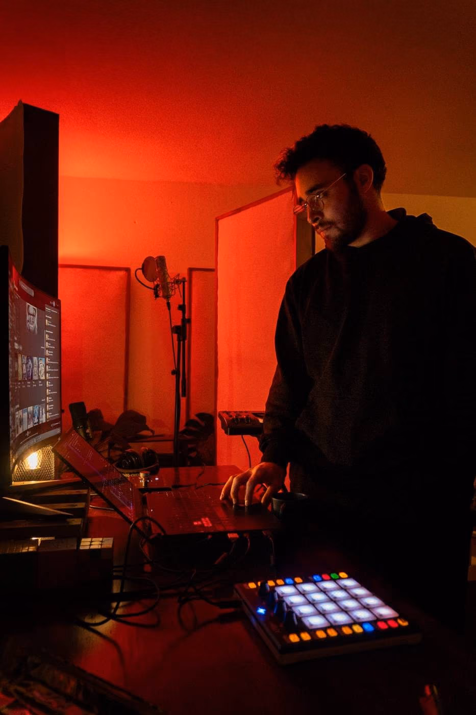 MATHIU en su escritorio de estudio bajo luz roja, con una laptop, un controlador de pads y un micrófono detrás.