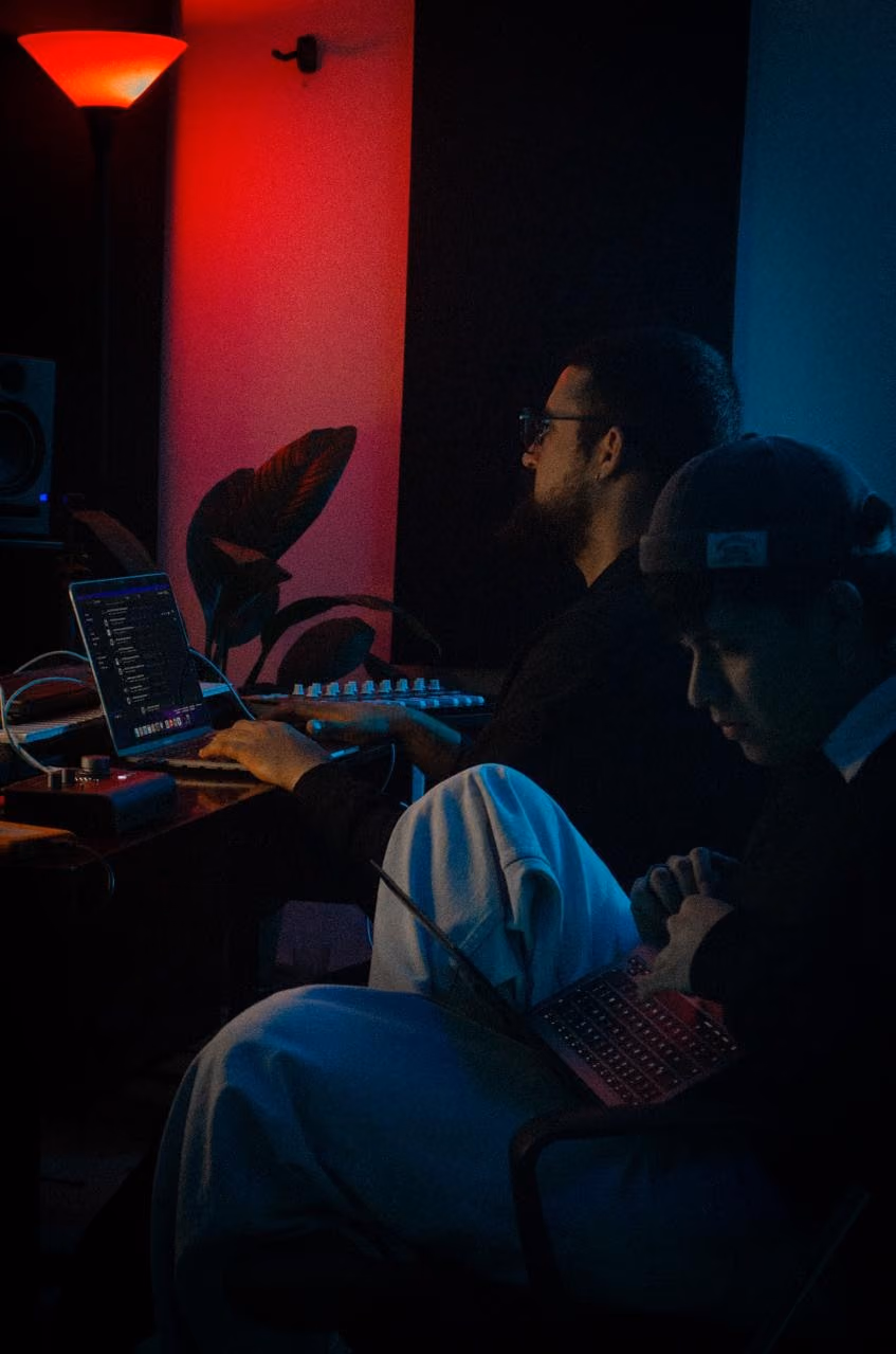 Dos personas trabajan en laptops en el estudio con luz roja y azul.