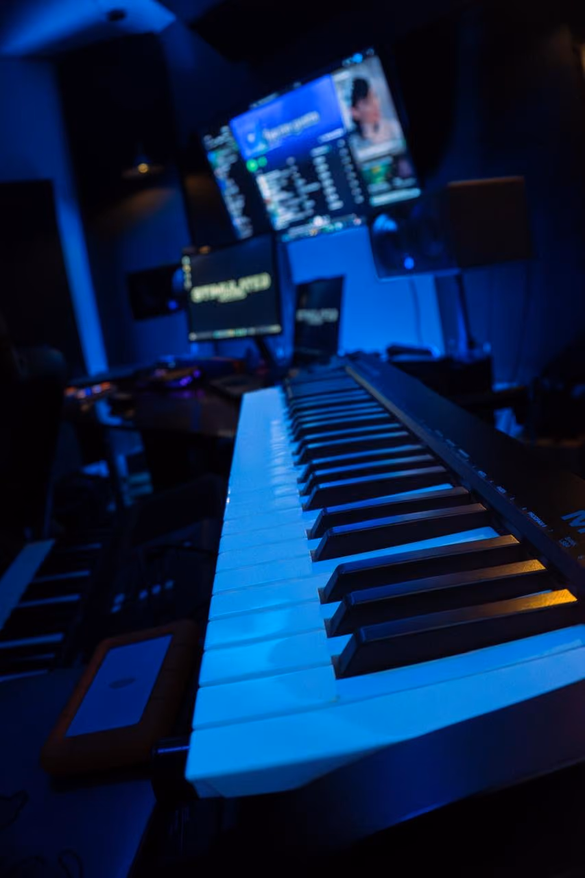 Primer plano de un teclado MIDI con luz azul y pantallas con el logo de Stimulated Records.