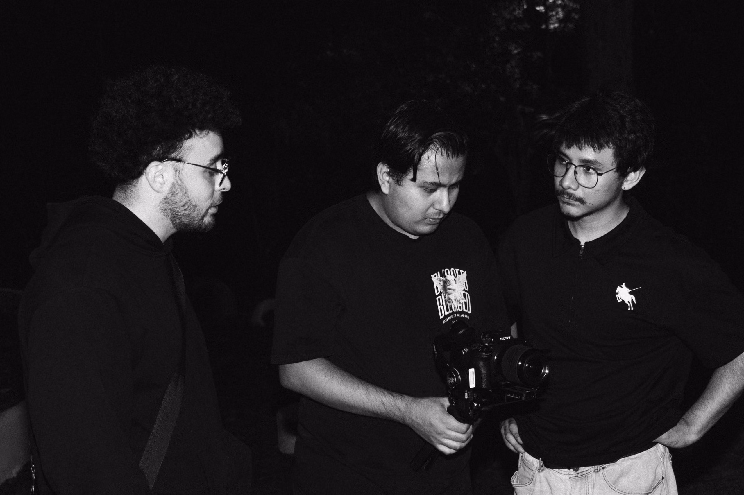 Tres personas revisan tomas en una cámara de noche, en blanco y negro.